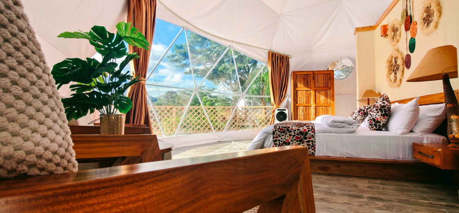 King bed dressed in white linen with carved headboard and woven wall art inside the dome